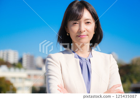 A confident middle-aged career woman in a white suit under a blue sky A confident middle-aged career woman in a white suit under a blue sky 125435087