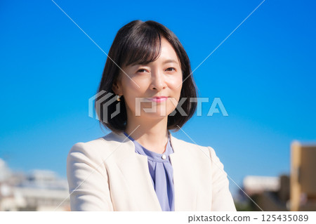 A confident middle-aged career woman in a white suit under a blue sky 125435089