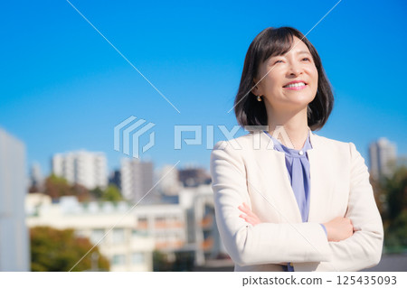 A confident middle-aged career woman in a white suit under a blue sky A confident middle-aged career woman in a white suit under a blue sky 125435093