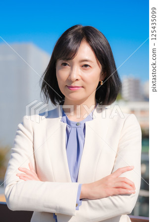 A confident middle-aged career woman in a white suit under a blue sky 125435099