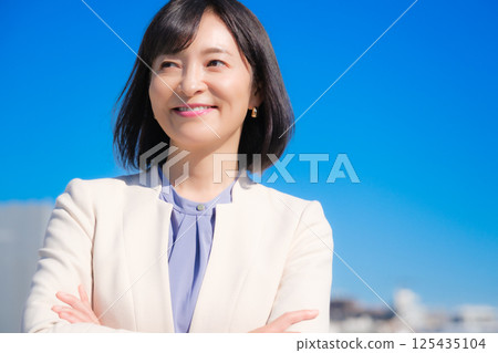 藍天下,一位自信的中年職業女性,身穿白色西裝 藍天下,一位自信的中年職業女性,身穿白色西裝 125435104
