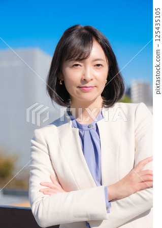 A confident middle-aged career woman in a white suit under a blue sky 125435105