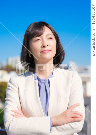 A confident middle-aged career woman in a white suit under a blue sky A confident middle-aged career woman in a white suit under a blue sky 125435107