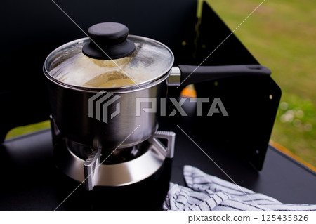 Stainless steel saucepan on portable stove with glass lid outdoors 125435826