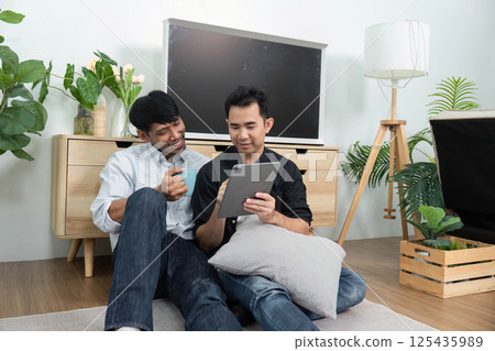 LGBTQ Bonding Moments. Two men engaged in a playful conversation while enjoying a tablet together. 125435989
