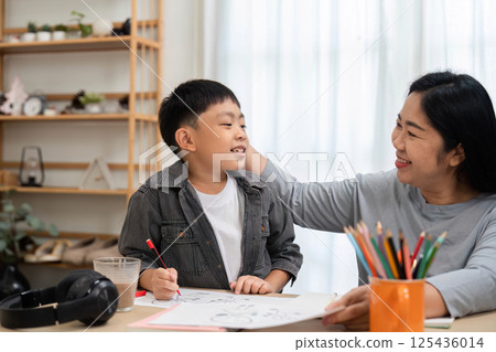 Learning and Bonding Time. A mother and her son share a joyful moment while drawing and engaging in creative activities. 125436014