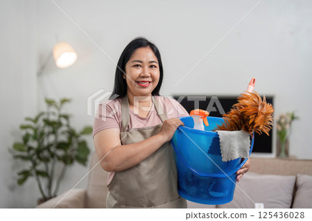 Cleaning and Home Maintenance. A woman smiling while holding a bucket of cleaning supplies. Cleaning and Home Maintenance. A woman smiling while holding a bucket of cleaning supplies. 125436028