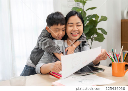 Learning and Togetherness. A mother and son share a moment of joy while looking at his drawing. 125436038