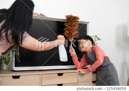 Home Cleaning and Family Bonding. A child helping his mother clean the living room with a duster and vacuum. Home Cleaning and Family Bonding. A child helping his mother clean the living room with a duster and vacuum. 125436059