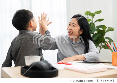 Back to School and Family Bonding. A mother and son share a joyful moment, high-fiving each other while preparing for school. Back to School and Family Bonding. A mother and son share a joyful moment, high-fiving each other while preparing for school. 125436061
