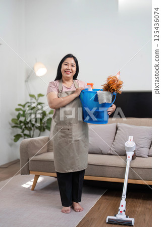 Cleaning Supplies and Home Care. A woman holding a bucket of cleaning supplies in her living room. 125436074