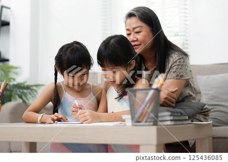 Learning and Family Bonding. Two young girls engage in creative activities while their grandmother assists them. 125436085