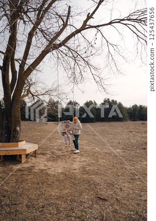 A man swings a girl on a swing in a field. A man swings a girl on a swing in a field. 125437656