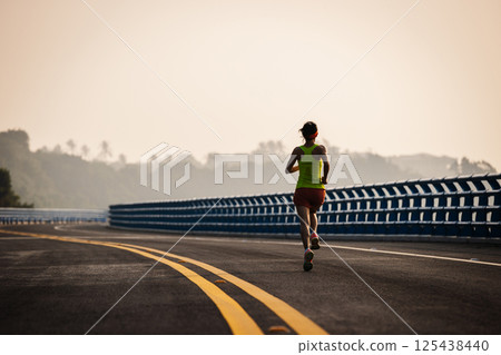 Asian fitness woman runner running on seaside bridge 125438440