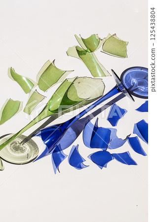 Broken Green and Blue Wine Glasses, Fragments Surrounding Them on White Background with Reflections and Harsh Shadow. Broken Green and Blue Wine Glasses, Fragments Surrounding Them on White Background with Reflections and Harsh Shadow. 125438804