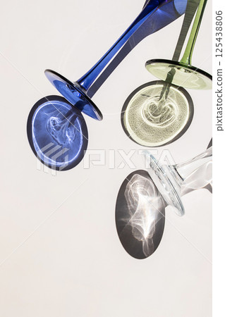Three Wine Glasses Lying on White Surface with Colorful Shadows and Sun Glare Visible. 125438806