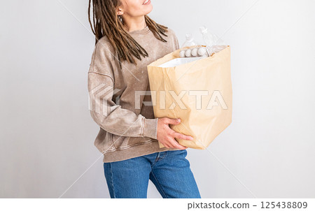 Woman with Dreadlocks Holding Paper Bag with Plastic Packing for Recycling. Environmental Concept for Earth Day. 125438809