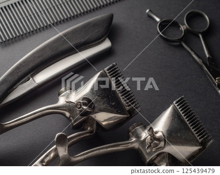 Antique barber tools are artfully placed on a dark surface, highlighting scissors, clippers, and a comb. This setup reflects the classic aspect of grooming and hairstyling. 125439479