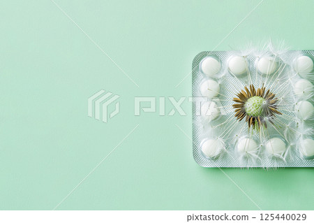 white dandelions on a blister pack of pills on light green background, allergy, herbal remedies 125440029