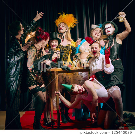 Cabaret cast celebrating around table with drinks and wild facial expressions in joyous vintage chaos. 125440089