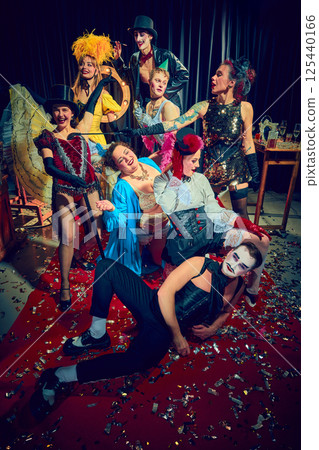 Cabaret troupe laughing and posing in exaggerated gestures under stage lights with expressive costumes and red carpet. Cabaret troupe laughing and posing in exaggerated gestures under stage lights with expressive costumes and red carpet. 125440166
