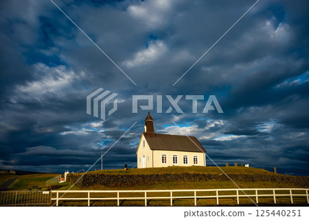 Wooden church Strandarkirkja with a steeple stands on a grassy hill in Iceland. Dramatic clouds fill the sky, creating a serene and picturesque landscape Wooden church Strandarkirkja with a steeple stands on a grassy hill in Iceland. Dramatic clouds fill the sky, creating a serene and picturesque landscape 125440251