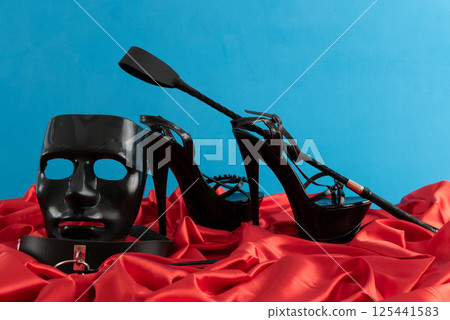 Adult sex games. Kinky lifestyle. Spank and a pair of black high-heeled shoes on the red linen. Bdsm outfit 125441583