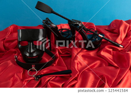 Adult sex games. Kinky lifestyle. Spank and a pair of black high-heeled shoes on the red linen. Bdsm outfit 125441584