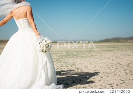A bride stands in the field with a bouquet in her hand 125442000