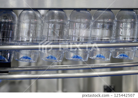 The empty drinking water bottles hanging on the overhead conveyor belt for filling process. The empty drinking water bottles hanging on the overhead conveyor belt for filling process. 125442507
