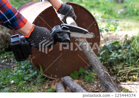 A man in gloves saws a wooden tree trunk with a saw. A man in gloves saws a wooden tree trunk with a saw. 125444374