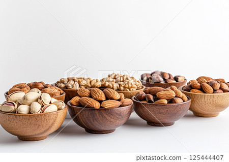 A variety of nuts and dried fruits arranged in wooden bowls on a light gray surface, showcasing a nutritious and colorful selection of healthy snacks. A variety of nuts and dried fruits arranged in wooden bowls on a light gray surface, showcasing a nutritious and colorful selection of healthy snacks. 125444407