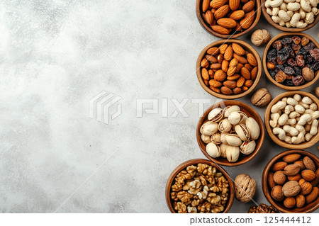 A variety of nuts and dried fruits arranged in wooden bowls on a light gray surface, showcasing a nutritious and colorful selection of healthy snacks. 125444412