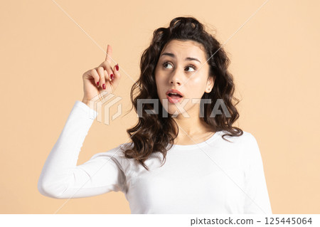 Woman pointing one finger up and looking aside the camera 125445064