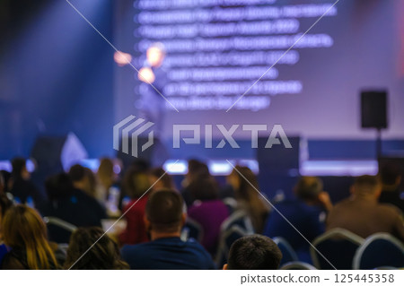 Audience in a conference room with speaker on stage presenting under spotlight Audience in a conference room with speaker on stage presenting under spotlight 125445358