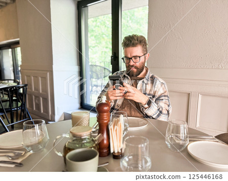 Man browsing phone at cafe table. Modern lifestyle, digital habits and casual urban dining 125446168