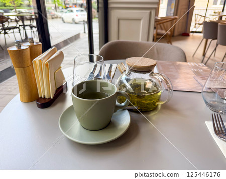 Hot green tea served at a cozy urban cafe table. Moment of pause, flavor and quiet enjoyment in the city Hot green tea served at a cozy urban cafe table. Moment of pause, flavor and quiet enjoyment in the city 125446176