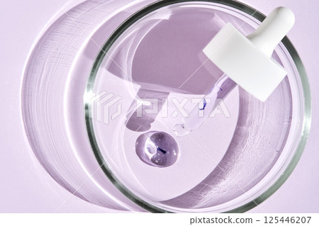 The texture of the serum and a cosmetic pipette in a petri dish on a purple background. 125446207