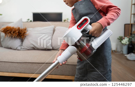 Child Learning and Cleaning. A child vacuuming the living room with a handheld vacuum. 125446297