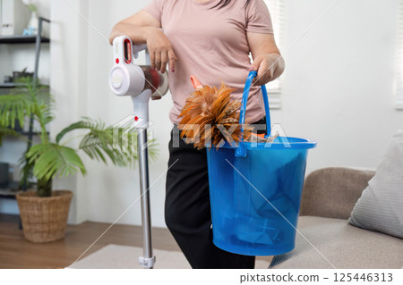Cleaning Tools and Household Chores. A person holding a bucket with cleaning supplies while vacuuming. 125446313