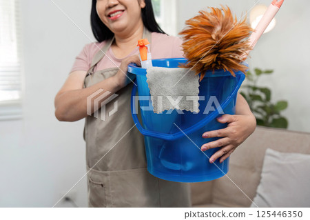 Cleaning Supplies and Home Care. A mother holds a bucket filled with cleaning tools, ready for house chores. 125446350