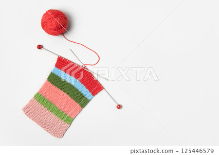 Striped piece of knitted fabric for future clothing with knitting needles and yellow ball of thread on gray background. Homemade needlework and knitting of warm, clothes and toys. Concept creativity 125446579