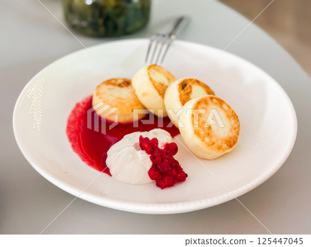 Syrniki served with sour cream and berry sauce. Traditional breakfast, rustic comfort and Eastern European cuisine Syrniki served with sour cream and berry sauce. Traditional breakfast, rustic comfort and Eastern European cuisine 125447045