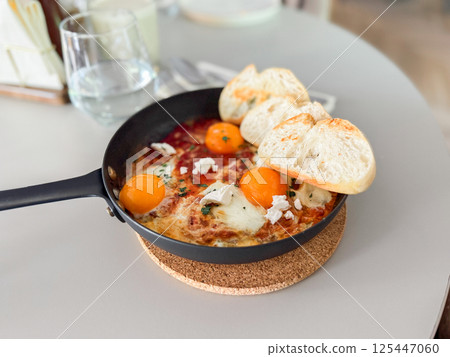 Shakshuka served hot in pan with bread slices. Comfort food, modern brunch and urban culinary style Shakshuka served hot in pan with bread slices. Comfort food, modern brunch and urban culinary style 125447060