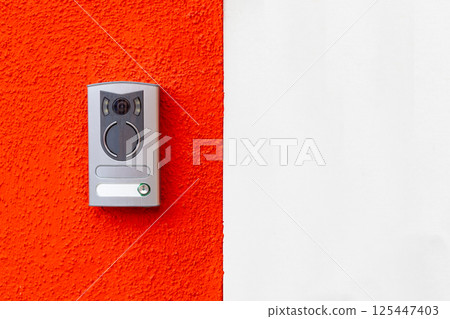 Modern door intercom on red and white wall 125447403