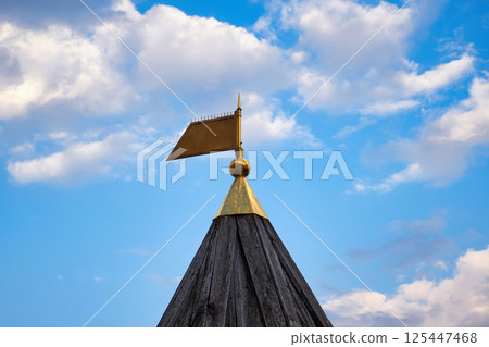 Golden flag finial on wooden tower against sky background Golden flag finial on wooden tower against sky background 125447468