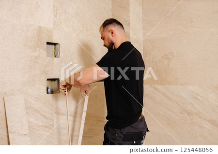 Construction worker installing ceramic tiles on bathroom wall using level tool Construction worker installing ceramic tiles on bathroom wall using level tool 125448056