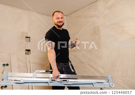Tiler carrying tile cutter in bathroom during renovation Tiler carrying tile cutter in bathroom during renovation 125448057