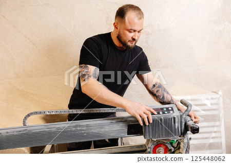 Construction worker using tile saw cutting machine preparing ceramic tiles for bathroom renovation Construction worker using tile saw cutting machine preparing ceramic tiles for bathroom renovation 125448062