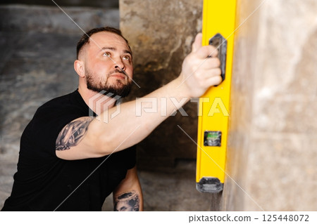 Construction worker using spirit level installing marble tile on wall 125448072